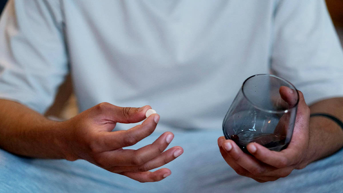 Person holding a pill and a glass of water