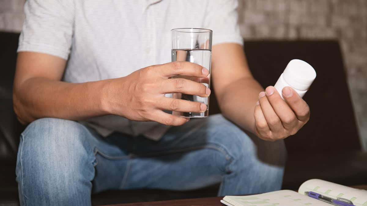 Person holding a bottle of pills and a glass of water